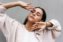 Безтурботний танцівниця слухає музику в навушниках і танцює із закритими очима, насолоджуючись піснями на тлі сірої стіни в місті — стокове фото