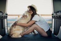 Barfüßige Frau umarmt treuen Golden Retriever Hund, während sie im Wohnmobil auf dem Bett sitzt, während sie in der Natur unterwegs ist — Stockfoto