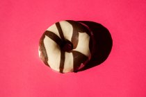 Rosquillas blancas recubiertas de chocolate oreo piezas de galletas sobre fondo rosa - foto de stock
