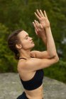 Side view of young female with closed eyes twisting arms while doing Garudasana pose in countryside — Stock Photo