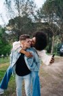 Junger Mann gibt fröhliche ethnische Freundin Huckepack-Fahrt gegen Wohnmobil und Thai Ridgeback auf Weg — Stockfoto
