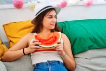 Positivo jovem mulher sentado à mesa com maduro suculento melancia e desfrutar de verão no quintal tenda — Fotografia de Stock