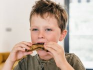 Entzückendes Kind isst appetitliche Schweinerippchen während des Mittagessens zu Hause und schaut weg — Stockfoto