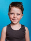 Contenuto adorabile ragazzo preadolescente guardando la fotocamera su sfondo blu brillante in studio — Foto stock