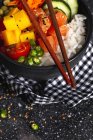 High angle of Asian poke with salmon and rice with assorted vegetables served in bowl on table with chopsticks in restaurant — Stock Photo