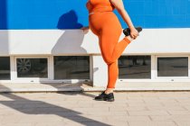 Side view of crop unrecognizable plump female athlete in sportswear exercising on tiled walkway in sunny town — Stock Photo