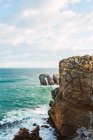 Захватывающий пейзаж грубого скалистого берега, омываемого пенными морскими волнами в солнечном свете под голубым облачным небом в Кантабрии Лиенкрес в Испании — стоковое фото