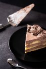 De dessus de morceau de délicieux gâteau au chocolat à la truffe servi dans une assiette sur une table noire avec cuillère et spatule — Photo de stock