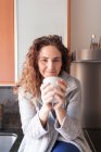 Woman with curly hair sitting in the kitchen taking an infusion — Stock Photo