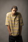 Young African American male model with braided hair dressed in oversized striped shirt and necklace looking at camera against gray background — Stock Photo