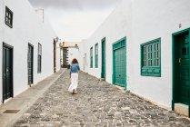 Rückansicht einer anonymen Frau in legerer Kleidung, die auf dem Steinpflaster in der Nähe weißer Häuser auf der Straße der Stadt in Fuerteventura, Spanien, spaziert — Stockfoto