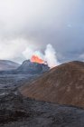 Pintoresca vista de Fagradalsfjall con fuego rápido y lava bajo humo difuso en montañas con nubes en Islandia - foto de stock