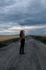 Стильна молода жінка торкається довгого волосся на проїжджій частині під хмарним небом в сутінках — стокове фото