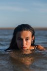 Donna serena con i capelli bagnati nuotare in mare calmo in estate sera e guardando la fotocamera — Foto stock