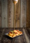 Salsa de queso vertiendo en el plato con papas fritas apetitosas y pimientos picantes colocados en la mesa de madera en el restaurante - foto de stock
