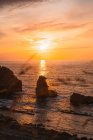 Amazing peaceful scenery of sunset over rippled wavy sea with rocks under colorful cloudy sky in summer evening in Liencres Cantabria Spain — Stock Photo