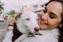 Encantada propietaria femenina abrazando al lindo perro Border Collie y sonriendo con los ojos cerrados - foto de stock