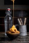 Käsesauce auf leckerem knusprigem Huhn auf Teller in der Nähe von Glasflasche mit Wasser im dunklen Restaurant platziert — Stockfoto