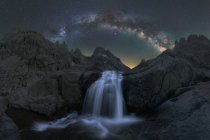 Magnífica paisagem de espuma salpicando cachoeira fluindo entre terreno rochoso áspero sob céu estrelado noite com brilhante brilhante Via Láctea — Fotografia de Stock