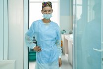 Весела доросла жінка-лікар у стерильній масці та декоративній шапці дивиться на камеру в лікарні — стокове фото