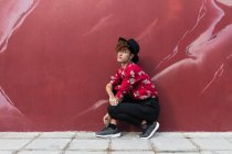 Вид збоку модний гомосексуальний чоловік з довгими цвяхами в декоративній сорочці, дивлячись на камеру, присідаючи на тротуарі на стіну — стокове фото
