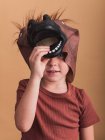 Ребенок в футболке и маске лошади на голове смотрит в камеру на бежевом фоне — стоковое фото