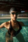 Giovane bella donna sul marciapiede della piscina coperta, con costume da bagno nero — Foto stock