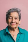 Donna anziana con capelli corti grigi e occhi marroni che guarda la fotocamera su sfondo rosa in studio — Foto stock