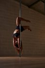 Graciosa mulher flexível dançando no poste e mostrando suporte durante o ensaio em estúdio — Fotografia de Stock