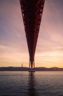 From below rusty metal mooring poles located on shore of Tagus River under 25 de Abril Bridge at sundown in Lisbon, Portugal — Stock Photo