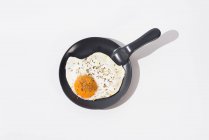 Вкусное жареное яйцо на черной сковороде подается на столе на белом фоне в студии — стоковое фото