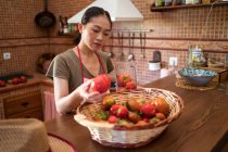 Enfocado ama de casa étnica seleccionar tomates frescos en la cocina mientras cocina alimentos en casa - foto de stock