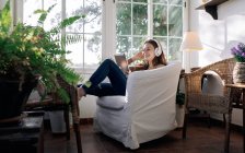 Content female in wireless headset browsing internet on tablet while listening to song in armchair at home — Stock Photo