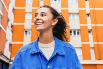 Low angle of cheerful female standing in street against bright building and laughing — Stock Photo