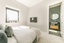 Interior de dormitorio contemporáneo con cama con almohadas suaves colocadas cerca de la ventana en el apartamento en estilo minimalista - foto de stock