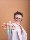 Astonished boy in eyeglasses and laboratory robe with dirty face and liquid in bottle after making chemical experiment — Stock Photo