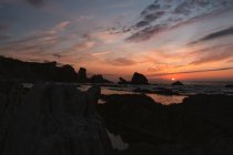 Paisagem pacífica incrível de pôr do sol sobre o mar ondulado ondulado ondulado com rochas sob o céu nublado colorido na noite de verão em Liencres Cantabria Espanha — Fotografia de Stock