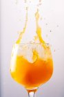 Освіжаючий апельсиновий коктейль, що бризкає у блискучому скляному горщику на сірому фоні в студії — стокове фото