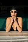 Mulher bonita jovem dentro da piscina interior, com maiô preto, esfaqueado na borda — Fotografia de Stock