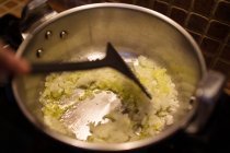 Сверху неузнаваемый повар жарит нарезанный чеснок и лук в металлической сковороде во время приготовления пищи на кухне дома — стоковое фото