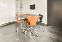 Round table and chairs placed in modern spacious room with TV hanging on white wall — Stock Photo