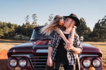 Pareja joven enamorada sentada en rojo vintage pickup y besándose al atardecer en verano - foto de stock