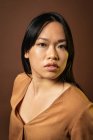 Vista frontal da mulher asiática em roupas da moda olhando para a câmera no fundo marrom em estúdio — Fotografia de Stock