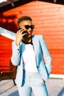 Весела афроамериканська жінка в модному костюмі з рукою в кишені розмовляє по мобільному, дивлячись в далекому сонячному місті. — стокове фото