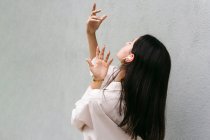 Безтурботний танцівниця слухає музику в навушниках і танцює із закритими очима, насолоджуючись піснями на тлі сірої стіни в місті — стокове фото