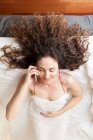 Вид зверху на ділову жінку з кучерявим волоссям, що лежить у ліжку, розмовляючи по телефону — стокове фото