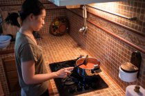 Сверху женщина добавляет соль в кастрюлю во время приготовления соуса маринара из помидоров на плите на кухне — стоковое фото