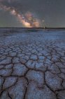Silhueta distante de explorador de pé e segurando uma lanterna na lagoa de sal seco no fundo do céu estrelado com brilhante Via Láctea à noite — Fotografia de Stock