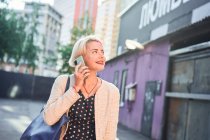 Fröhliche alternative Frau mit kurzen Haaren steht in der Stadt und spricht mit dem Handy — Stockfoto