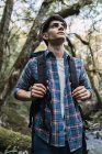 Vista laterale di viaggiare uomo con zaino in piedi su strada sabbiosa nella foresta durante il trekking e guardando lontano — Foto stock